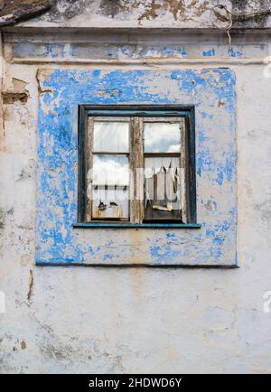 Vita morta di un muro con finestra derelitto con semplice cartouche blu sbiadito e vernice sfaldante su una tapparella di legno. Portogallo. Foto Stock