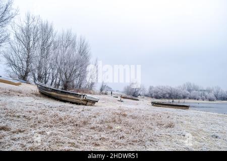 Una barca da pesca di legno tirò fuori sulla riva del affluente del Danubio in acqua ghiacciata. Foto Stock