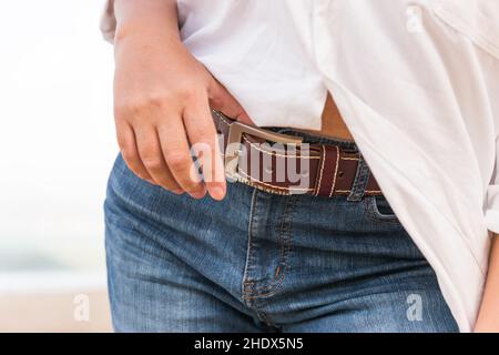 Una donna in pantaloni blu e una camicia bianca ha bottonato una cintura pantaloni marrone in pelle. Foto Stock