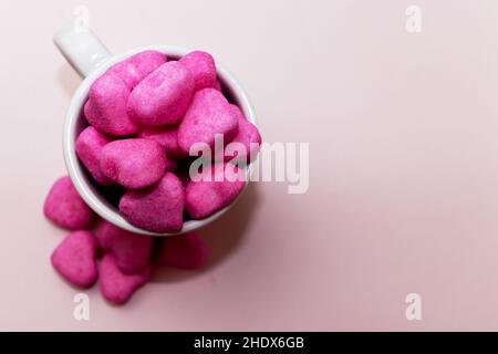 Un mucchio di caramelle rosa a forma di cuore in una tazza bianca su sfondo rosa Foto Stock