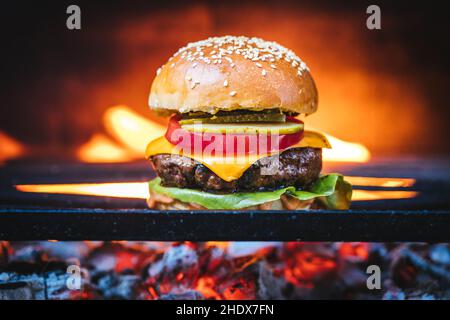 Hamburger classico succosa su una griglia barbecue a carbone con fuoco naturale sullo sfondo. Hamburger di formaggio dall'aspetto naturale. Foto Stock