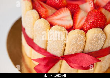 torta al tiramisù da vicino con fragole, savoiardi, mascarpone e nastro di prua rosso su bianco Foto Stock