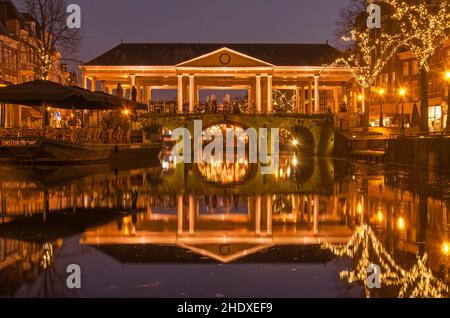 Leiden, Paesi Bassi, 16 dicembre 2021: Lo storico Koornbeurs (Corn Exchange) attraverso il canale Nieuwe Rijn nell'ora blu in una ventata invernale Foto Stock