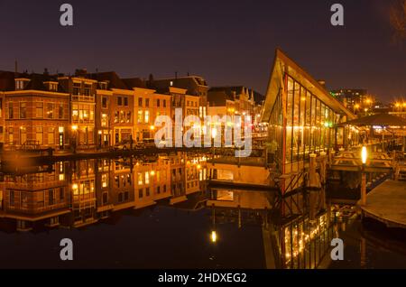 Leiden, Paesi Bassi, 16 dicembre 2021: Case e caffetterie che si riflettono nelle acque fluide del canale Oude Vest in una notte invernale senza vento Foto Stock