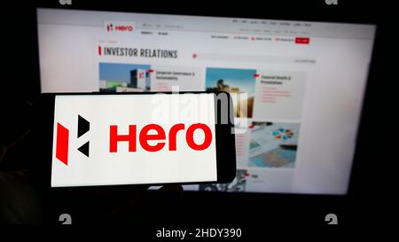 Persona che tiene il cellulare con il logo della società automobilistica indiana Hero MotoCorp Limited sullo schermo di fronte al sito web. Mettere a fuoco sul display del telefono. Foto Stock