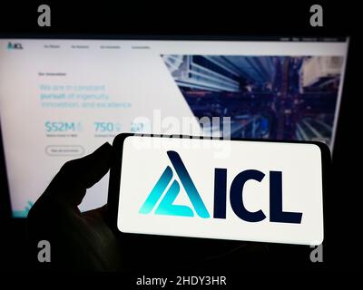 Persona che tiene il cellulare con il logo della società chimica israeliana ICL Group Ltd. Sullo schermo di fronte al sito web aziendale. Mettere a fuoco sul display del telefono. Foto Stock