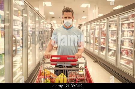 consumo. negozio durante quarantena. uomo in maschera di protezione con carrello. Foto Stock