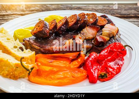 Bistecca club con salsicce alla griglia e peperoni dolci su piatto bianco con luce del sole Foto Stock