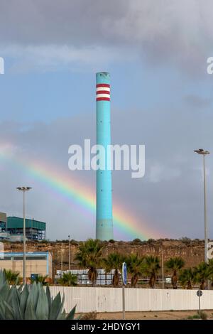 Arcobaleno nel cielo tempestoso dietro l'alto camino industriale cementificio blu, Carboneras, Almeria, Spagna Foto Stock