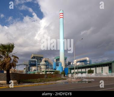 Arcobaleno nel cielo tempestoso dietro l'alto camino industriale cementificio blu, Carboneras, Almeria, Spagna Foto Stock