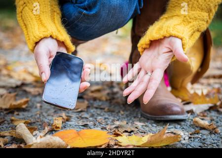 Donna sconvolto e smartphone rotto. Donna che raccoglie il telefono cellulare danneggiato da terra. Foto Stock