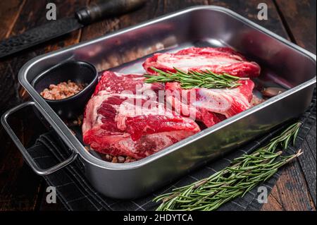 Costolette di manzo crudo in vassoio d'acciaio con rosmarino. Sfondo in legno. Vista dall'alto Foto Stock