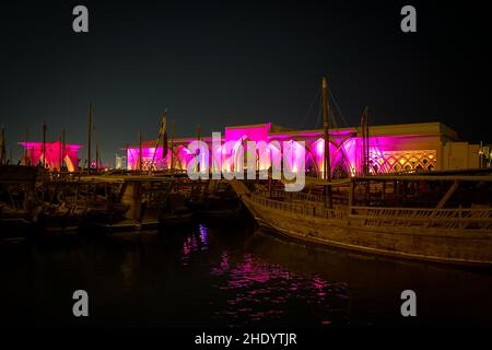 Le tradizionali barche in legno chiamate Dhows di fronte alla sala illuminata al Sukyum di Doha di notte, Qatar, Medio Oriente di fronte al cielo scuro e limpido Foto Stock