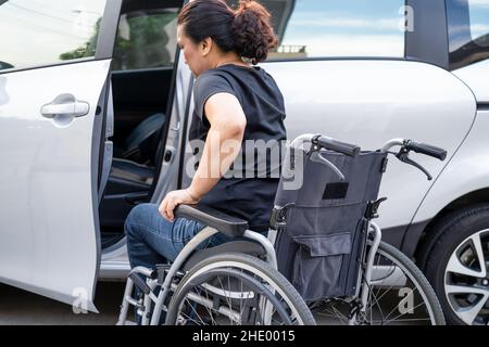 Donna asiatica pieghevole e sollevare la sedia a rotelle nella sua auto. Concetto di accessibilità. Foto Stock