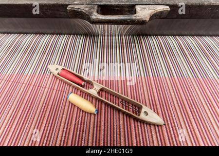 Telaio di tessitura tradizionale tailandese in legno e navetta di tessitura con colori filo da cucire su cotone tessuto. Primo piano. Vista dall'alto. Foto Stock