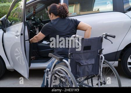 Donna asiatica pieghevole e sollevare la sedia a rotelle nella sua auto. Concetto di accessibilità. Foto Stock