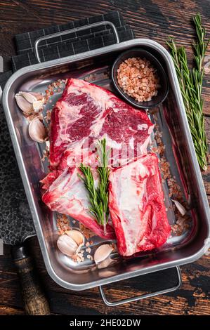 Costolette di manzo crudo in vassoio d'acciaio con rosmarino. Sfondo in legno. Vista dall'alto Foto Stock