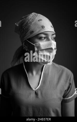 Ritratto intimo interno di latina donna salute operatore che indossa una maschera e una nutrice cappuccio durante la pandemia di Covid-19 Foto Stock