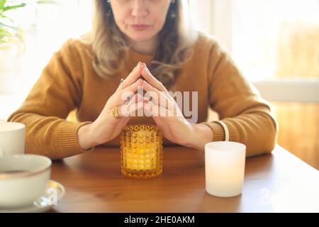 Immagine sfocata di donna seduta al tavolo che tiene bruciante candela profumata, femmina che crea l'atmosfera accogliente sul posto di lavoro. Pratica meditatio di consapevolezza Foto Stock