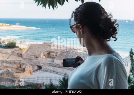 Donna dalla schiena scattando una foto con lo smartphone ad un monumento Foto Stock