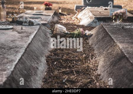 Un vaso di vetro rovesciato e invecchiato con un garofano siede ad una tomba in un cimitero Foto Stock