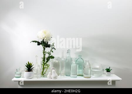 il crisantemo bianco in vaso di vetro con bottiglie di diverse forme con acqua si trova sulla cassettiera. Spazio di copia Foto Stock