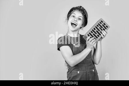 Artigiano o operaio professionale. Giornata internazionale dei lavoratori. Ragazza in casco gioca costruttore con mattone. Costruzione di una casa. Costruzione del capretto Foto Stock