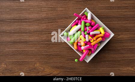 Vista dall'alto Sprinkles colorati che cadono su ciotola di porcellana bianca e tavola di legno 3D illustrazione Foto Stock