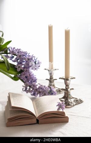 libro aperto e due candele su un tavolo con fiori di primavera Foto Stock