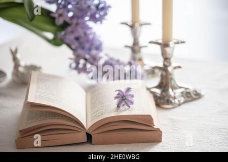libro aperto e due candele su un tavolo con fiori di primavera Foto Stock