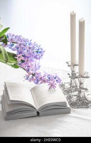 libro aperto e due candele su un tavolo con fiori di primavera Foto Stock