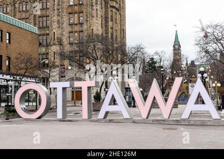 Ottawa, Canada - 17 dicembre 2021: Ottawa segno in centro a Byward Market in inverno, Torre della Pace del Parlamento con bandiera canadese in background Foto Stock