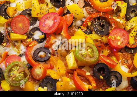 dettaglio dei condimenti su una pizza fatta in casa con olive, pomodori, peperoni, peperoni, erbe aromatiche, salsa di pomodoro, e formaggio Foto Stock