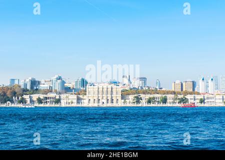 Il palazzo Dolmabahce si apre sul mare con il traghetto turistico rosso e bianco intorno e l'area del quartiere di Besiktas sullo sfondo. Istanbul, Turchia. H Foto Stock