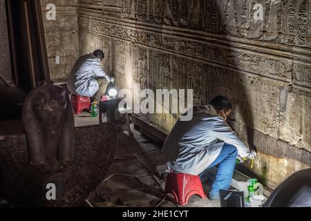 Restauratori conservatori che lavorano per riparare e ripristinare antiche pareti in pietra egiziana ricoperte di geroglifici e sculture in rilievo in un sito storico. Foto Stock