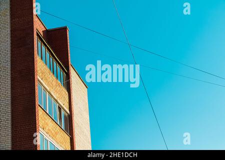 Una parte della facciata in mattoni dell'edificio di appartamenti e cavi sullo sfondo del cielo limpido in giorno di sole Foto Stock