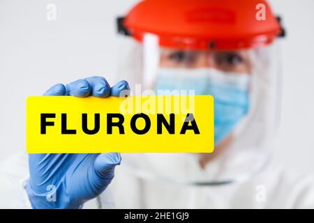 Mutazione genetica di Coronavirus che causa nuovi casi COVID-19, operatore medico che indossa PPE e visiera che tiene giallo scheda SARS-COV-2 segno FLURONA Foto Stock