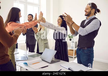 Le donne d'affari felici si danno cinque alti mentre i colleghi diversi stanno applaudendo Foto Stock
