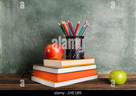 Una pila di libri e forniture per ufficio e due mele sullo sfondo del consiglio scolastico. Istruzione e concetto di ritorno a scuola. Foto Stock