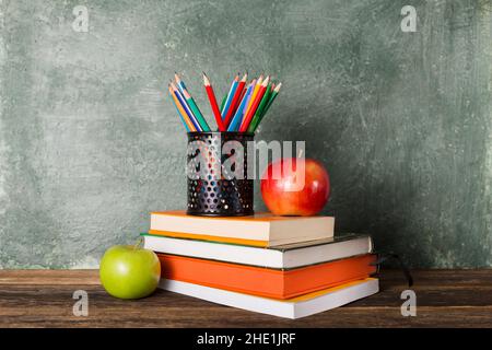 Una pila di libri e forniture per ufficio e due mele sullo sfondo del consiglio scolastico. Istruzione e concetto di ritorno a scuola. Foto Stock