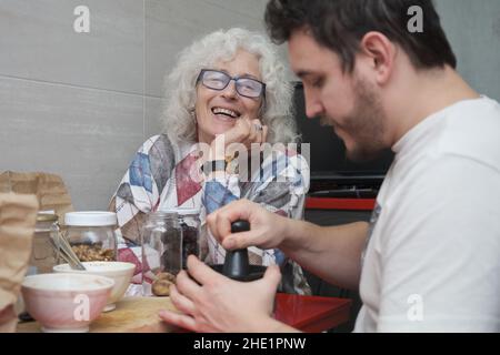 Madre matura ridendo mentre è in cucina con il suo figlio adulto. Foto Stock