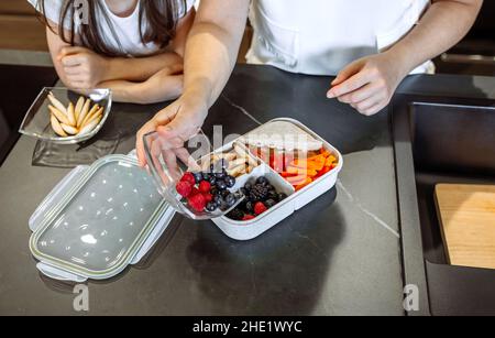 Ragazza che guarda la madre che mette il cibo nella sua scatola del pranzo Foto Stock