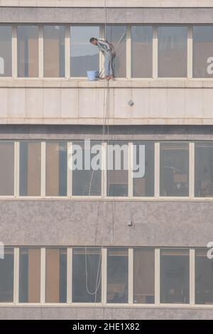 Una lavafinestre al Cairo, Egitto lavora per pulire il vetro di un alto edificio molti piani in su. Lavori pericolosi con attrezzatura di sicurezza minima. Foto Stock