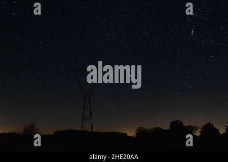 È notte, ed è oscurità impenetrabile. Potete vedere le stelle in un cielo senza nuvole. C'è un alto polo elettrico in metallo contro il cielo. Foto Stock