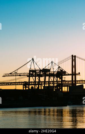 Silhouette di gru al porto di Lisbona, Portogallo, con il ponte del 25 aprile sullo sfondo al tramonto Foto Stock