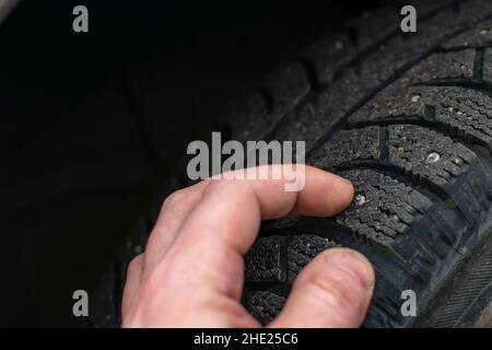 la mano di una persona, il conducente della vettura, tocca e controlla le condizioni dei picchi sugli pneumatici invernali Foto Stock