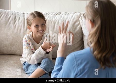 Bambino piccolo felice usando il linguaggio dei segni, comunicante con la madre. Foto Stock