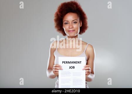 Felice giovane donna nera sucessful nominata ad un lavoro permanente che tiene il contratto davanti a lei mentre sorride alla macchina fotografica Foto Stock