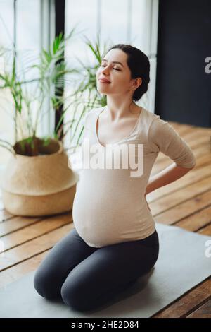 Meditazione durante la gravidanza. Giovane calma tranquilla donna incinta che fa yoga a casa, meditando e praticando la consapevolezza, madre in attesa seduta Foto Stock