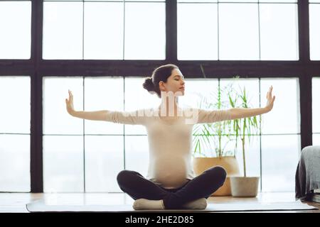 Meditazione durante la gravidanza. Giovane calma tranquilla donna incinta che fa yoga a casa, meditando e praticando la consapevolezza, madre in attesa seduta Foto Stock